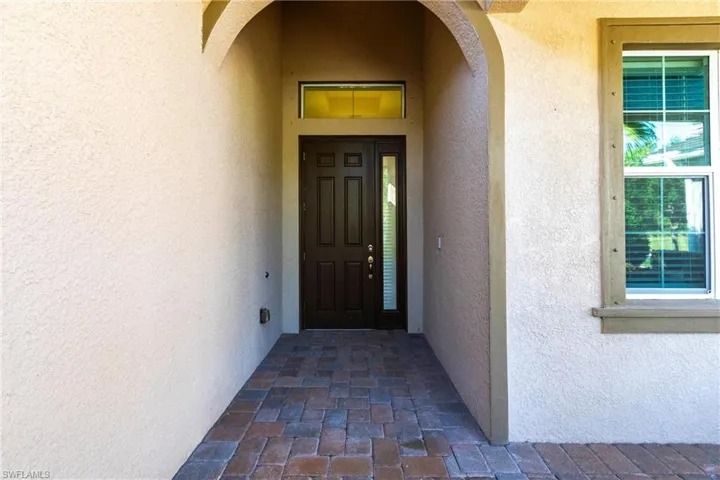 Covered entry featuring a dark paneled door with a sidelight, a transom window, and a brick paver pathway