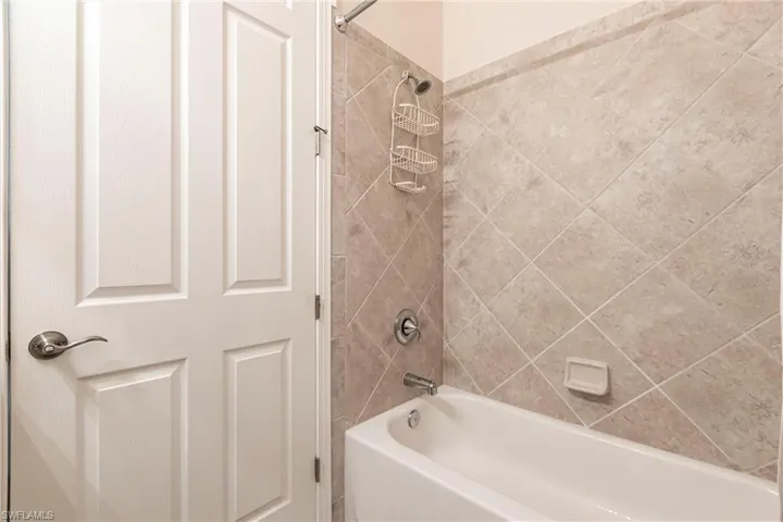 White bathtub featuring a shower with diagonal tile surround and brushed nickel fixtures