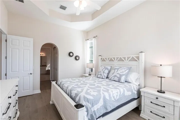 Bedroom featuring a tray ceiling with a ceiling fan, wood-finish flooring, and an arched doorway