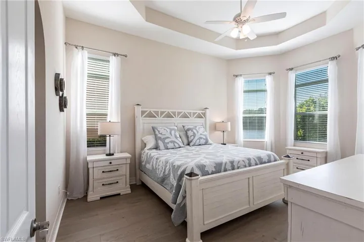 Recessed tray ceiling with ceiling fan, multiple windows with blinds and sheer curtains, wood-finish flooring, and arched doorway