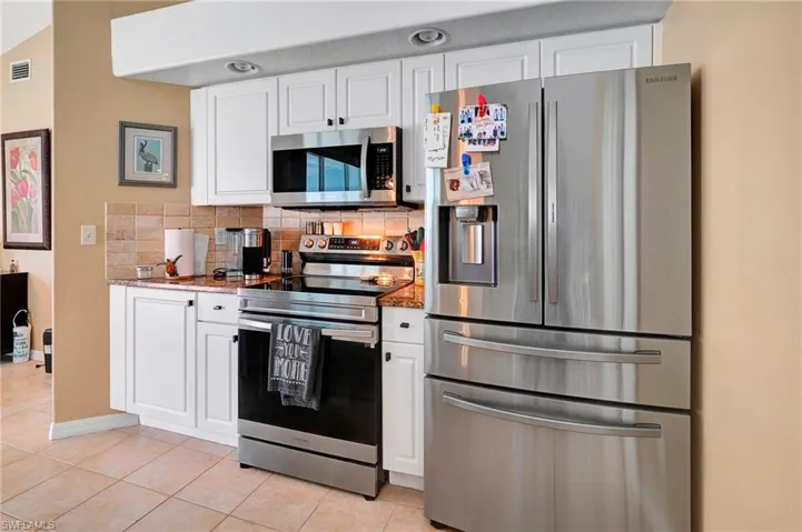 Kitchen with decorative backsplash, white cabinetry, stone countertops, light tile patterned floors, and stainless steel appliances