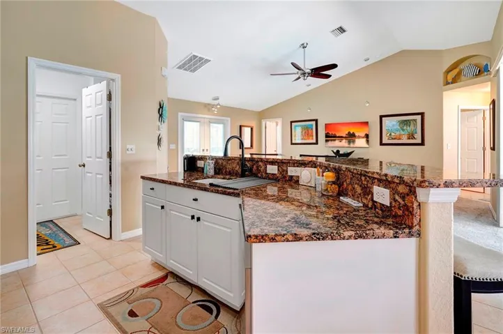 Kitchen featuring light tile patterned floors, dark stone countertops, ceiling fan, white cabinetry, and lofted ceiling