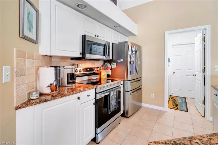 Kitchen featuring white cabinets, decorative backsplash, appliances with stainless steel finishes, and light tile patterned floors