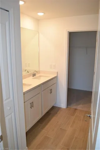 Full bath with double vanity, wood finish floors, and a walk in closet