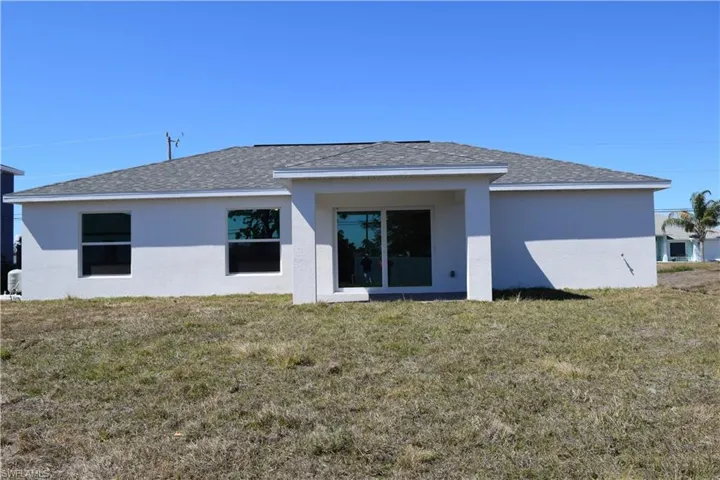 Rear view of house with a shingled roof, stucco siding, and a lawn