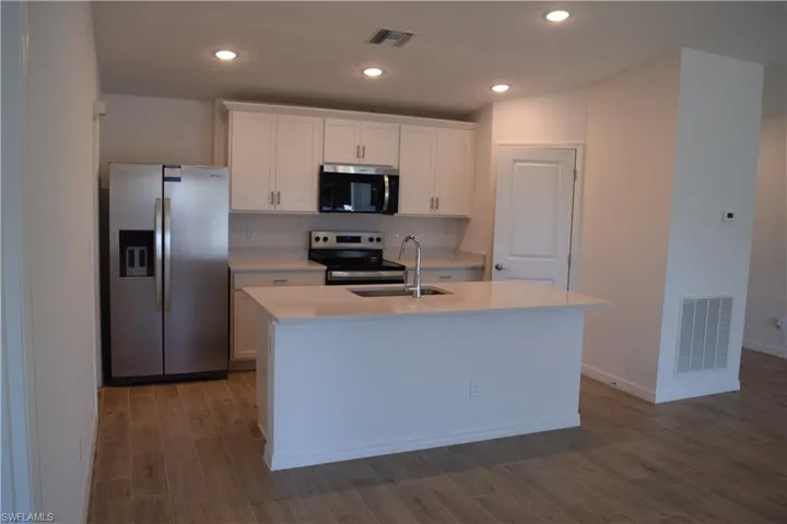 Kitchen with stainless steel appliances, white cabinetry, recessed lighting, dark wood-style flooring, and a center island with sink