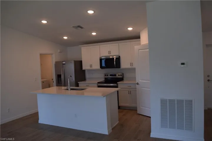 Kitchen featuring white cabinetry, stainless steel appliances, dark wood-style floors, recessed lighting, and a center island with sink