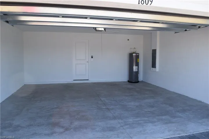 Garage with concrete block wall, water heater, and electric panel