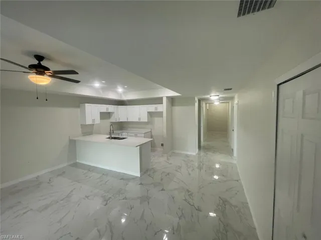 Kitchen with white cabinets, ceiling fan, sink, and kitchen peninsula