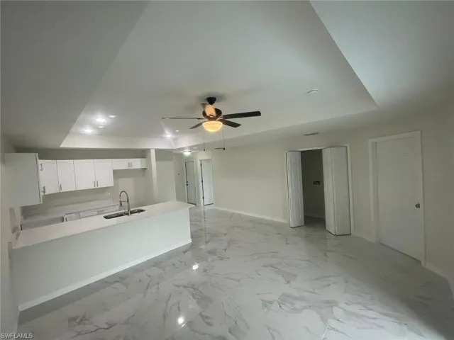 Kitchen with white cabinets, kitchen peninsula, sink, ceiling fan, and a tray ceiling