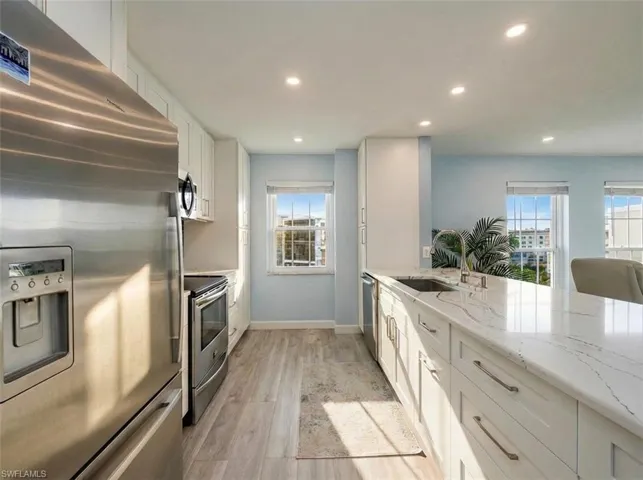Kitchen featuring stainless steel appliances, white cabinets, light stone counters, light wood finished floors, and recessed lighting