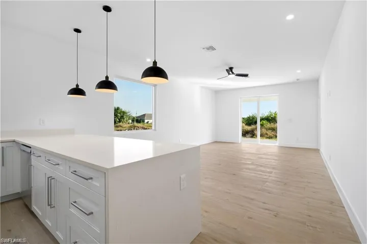 Kitchen featuring pendant lighting, dishwasher, white cabinetry, light hardwood / wood-style floors, and kitchen peninsula