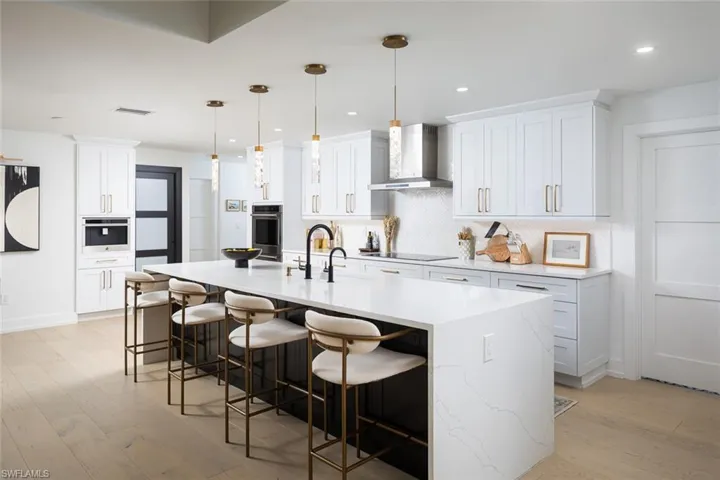 Kitchen with white cabinets, hanging light fixtures, and wall chimney range hood