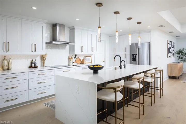 Kitchen featuring range hood, a kitchen island with sink, light wood-type flooring, high quality fridge, and white cabinetry
