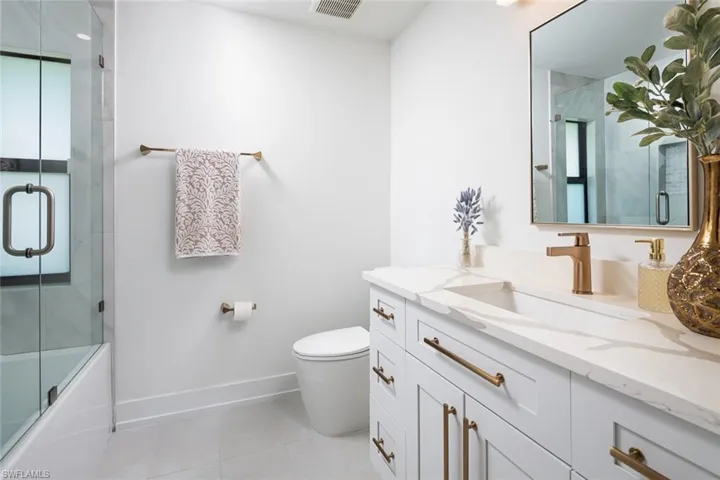 Full bathroom with a wealth of natural light, vanity, enclosed tub / shower combo, tile patterned floors, and toilet