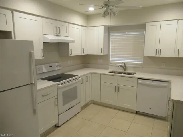 Kitchen featuring white appliances, white cabinetry, ceiling fan, light tile patterned flooring, and light stone counters