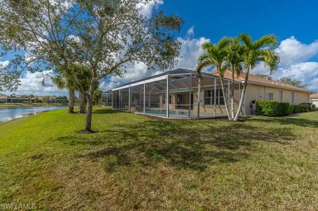 Back of house with a water view, a yard, and a lanai