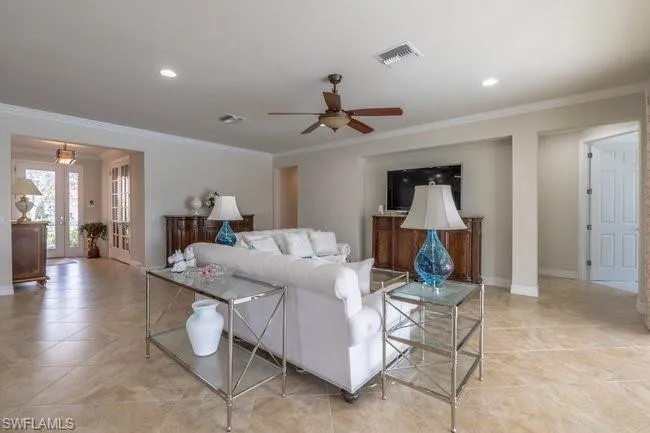 Living room with light tile patterned floors, ornamental molding, and ceiling fan