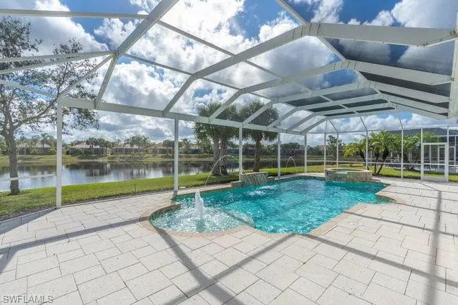 View of pool with a patio, a water view, glass enclosure, pool water feature, and an in ground hot tub