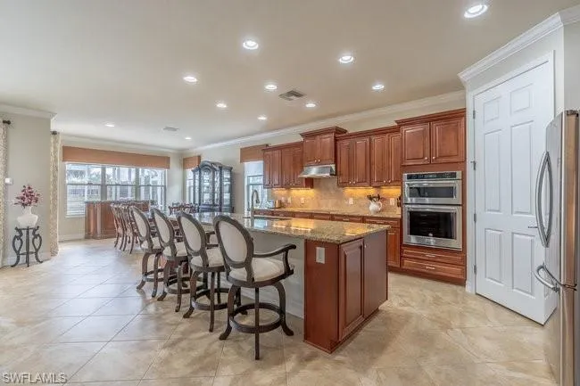 Kitchen with a center island with sink, stainless steel appliances, tasteful backsplash, a kitchen bar, and dark stone counters