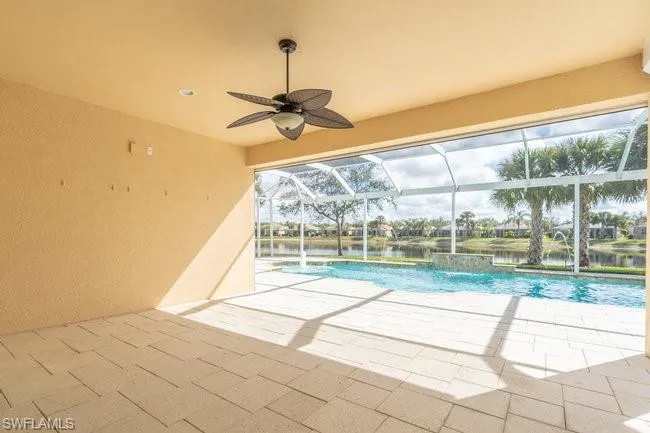 View of pool with pool water feature, a water view, a lanai, ceiling fan, and a patio