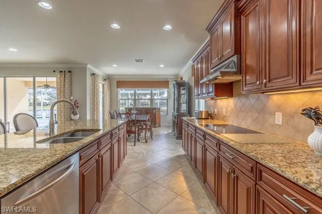 Kitchen featuring dishwasher, light stone countertops, sink, and black electric cooktop