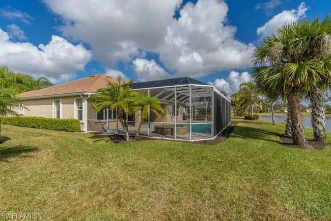 Rear view of house with a water view, a yard, a swimming pool, and glass enclosure