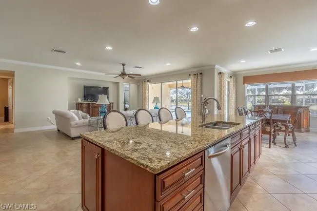 Kitchen featuring sink, ornamental molding, light stone countertops, a center island with sink, and stainless steel dishwasher