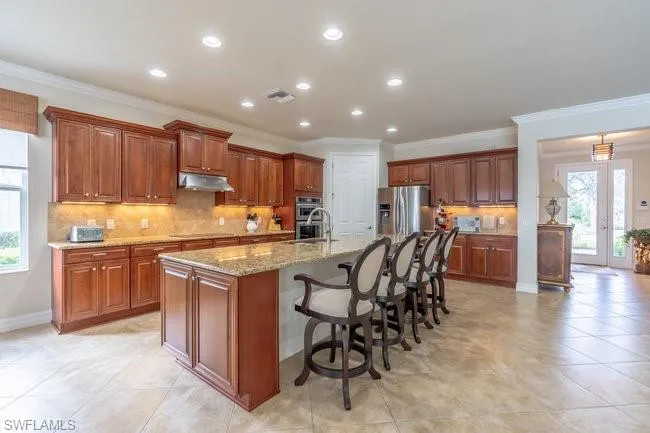 Kitchen with stainless steel appliances, a kitchen island with sink, a wealth of natural light, and a kitchen bar