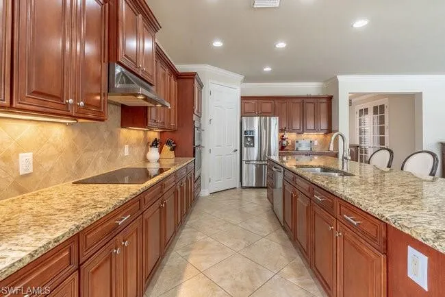 Kitchen featuring sink, light stone counters, stainless steel fridge with ice dispenser, crown molding, and black electric cooktop