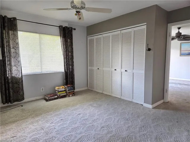 Carpeted interior space featuring a window with horizontal blinds, decorative curtains, and a white louvered bifold closet door system