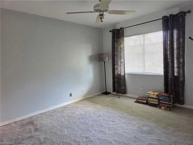 Spacious interior room featuring light gray walls, patterned carpeting, and a ceiling fan with integrated lighting