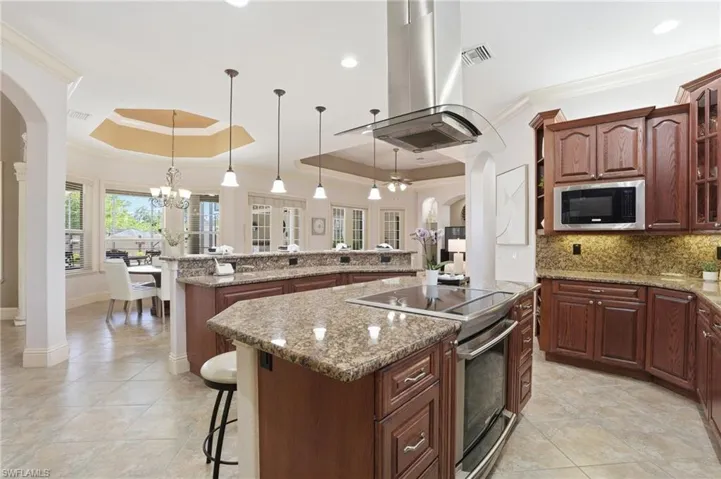 Gourmet kitchen featuring a large central island with a built-in cooktop, stainless steel range hood, granite countertops, wood cabinetry, and tile flooring