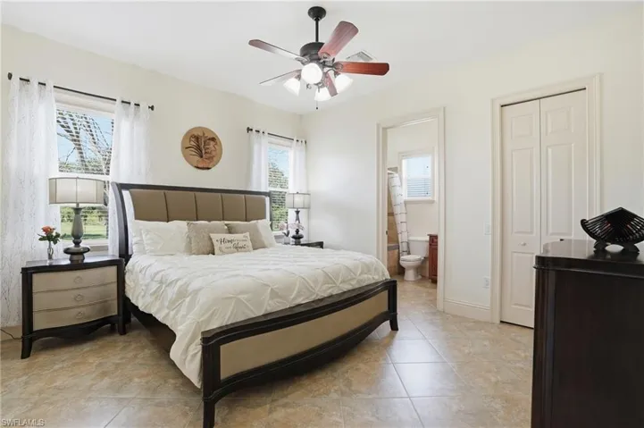 Spacious bedroom featuring multiple windows, neutral wall tones, tile flooring, and a ceiling fan
