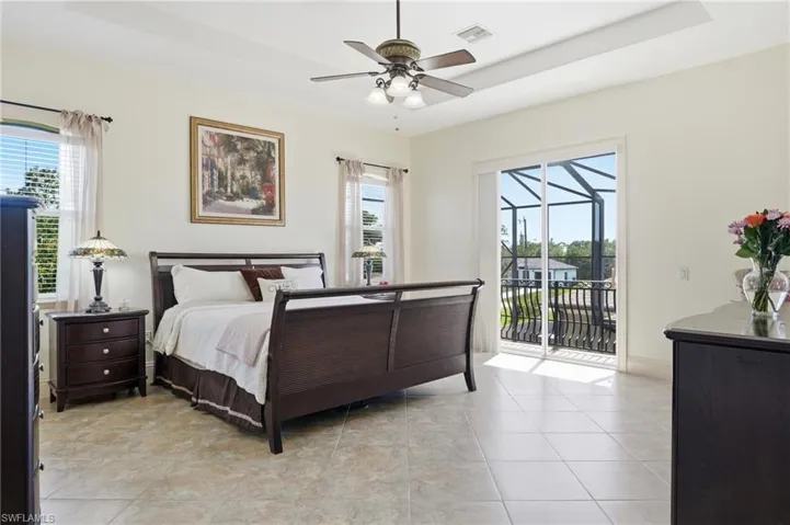 Bedroom featuring tile flooring, ceiling fan, white walls, and a sliding glass door opening to a private screened balcony with an ornate railing