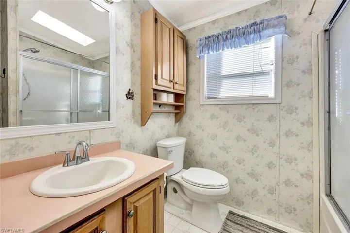 Bathroom with wallpapered walls, vanity, a skylight, light tile patterned flooring, and bath / shower combo with glass door
