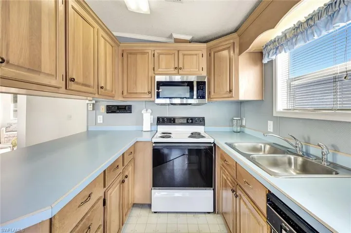 Kitchen featuring white range with electric stovetop, stainless steel microwave, light countertops, black dishwasher, and light flooring