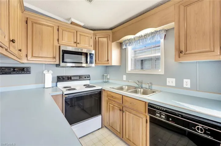 Kitchen with white electric stove, black dishwasher, light countertops, stainless steel microwave, and light brown cabinets