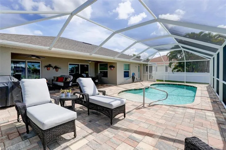 View of pool featuring glass enclosure, ceiling fan, an outdoor living space, and a patio area