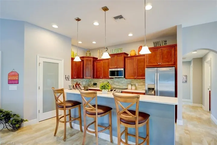 Kitchen with decorative backsplash, appliances with stainless steel finishes, a breakfast bar area, and decorative light fixtures