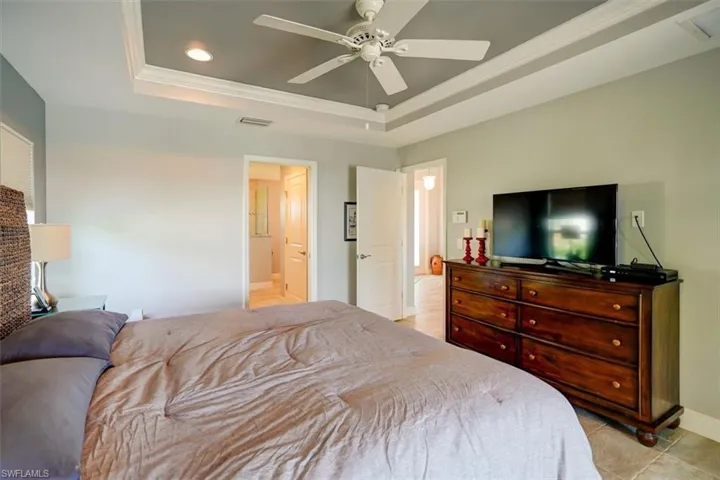 Tiled bedroom with connected bathroom, crown molding, ceiling fan, and a raised ceiling