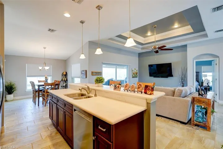 Kitchen featuring decorative light fixtures, a raised ceiling, sink, dishwasher, and a kitchen island with sink