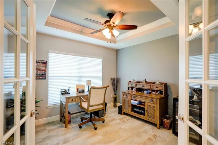 Office space featuring a tray ceiling, french doors, ceiling fan, and crown molding