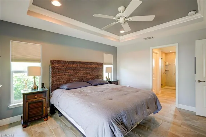 Bedroom featuring crown molding, ensuite bath, ceiling fan, and a raised ceiling