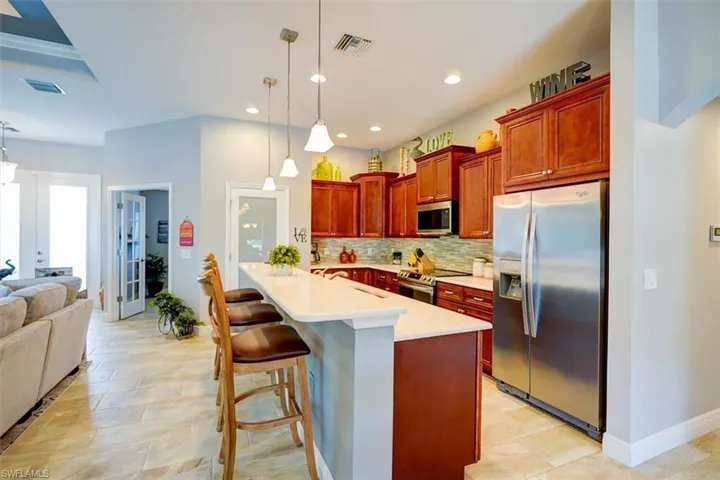 Kitchen featuring french doors, hanging light fixtures, tasteful backsplash, a kitchen breakfast bar, and appliances with stainless steel finishes
