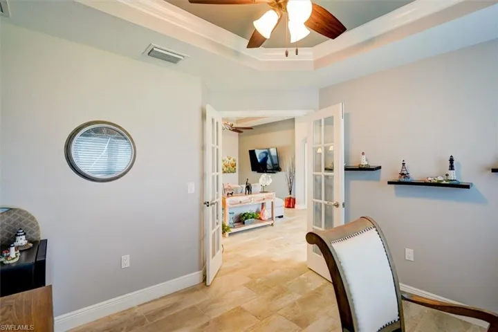 Home office with ceiling fan, a raised ceiling, and french doors