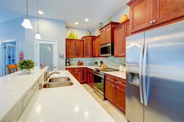 Kitchen with appliances with stainless steel finishes, sink, light stone counters, and hanging light fixtures