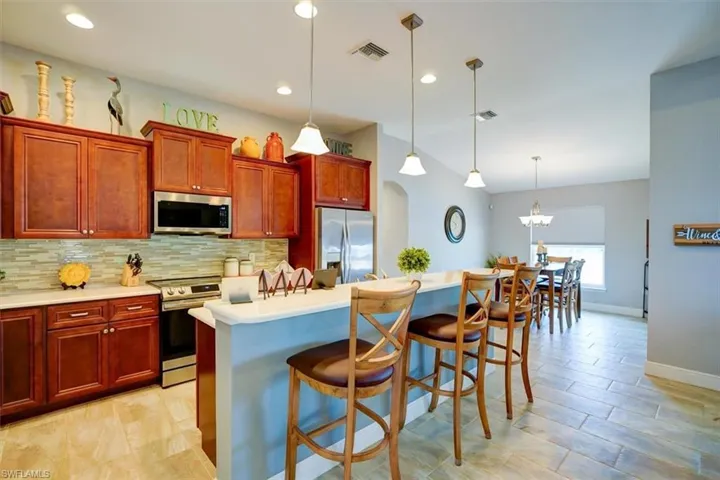 Kitchen featuring stainless steel appliances, decorative backsplash, hanging light fixtures, a breakfast bar area, and a kitchen island with sink