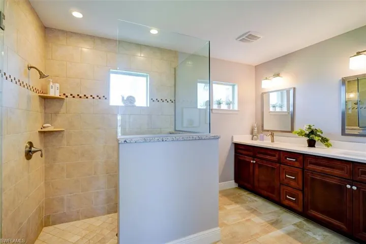 Bathroom with vanity, a tile shower, and a healthy amount of sunlight