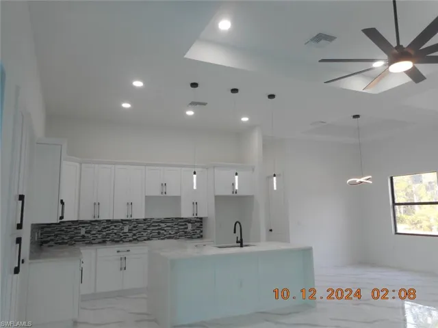 Kitchen featuring hanging light fixtures, an island with sink, white cabinets, and backsplash